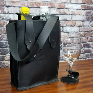 A double bottle wine bag in black leather with black suede side panels with an optional matching wine glass coaster on a stemmed wine glass 