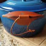 A side view of a brown leather cast iron assist handle holder showing fingertip protection down the side of a Dutch oven