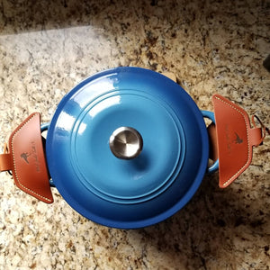 A set of brown leather cast iron handle holders on a blue Dutch oven