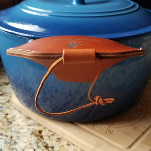 Side view of brown leather assist handle holder shown on blue dutch oven to show fingertip protection