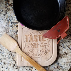 A brown leather assist handle holder on a black cast iron skillet shown with a cutting board and wooden spoon